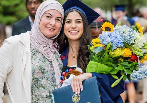 New graduate holding flowers with relative.